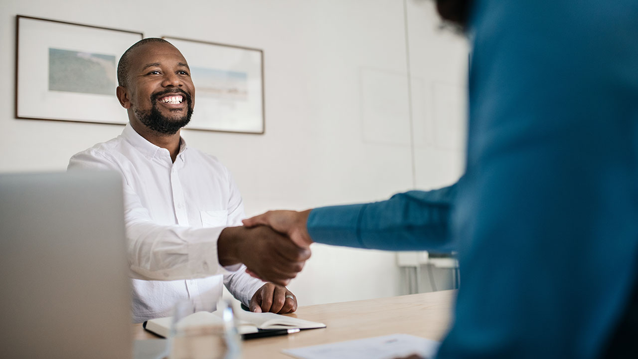 Interviewer and interviewee shaking hands at a desk